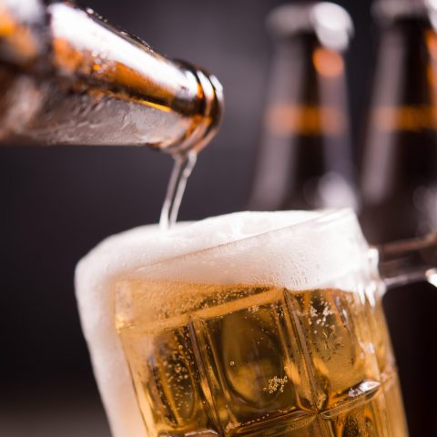 Glass bottles of beer with glass and ice on dark background